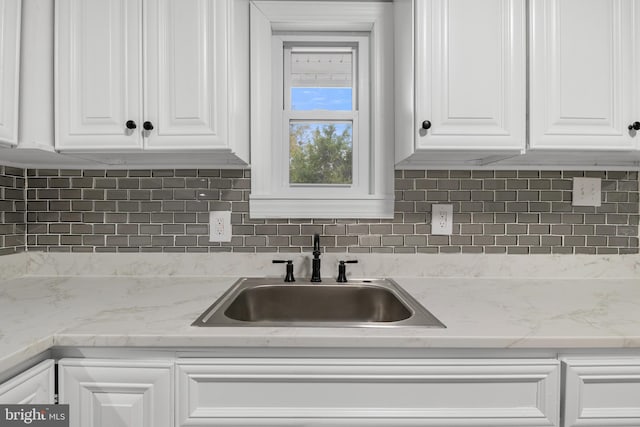 kitchen featuring backsplash, light stone countertops, sink, and white cabinets