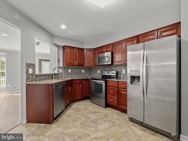 kitchen with light stone counters, backsplash, sink, appliances with stainless steel finishes, and a textured ceiling