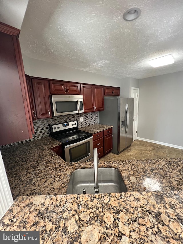 kitchen with decorative backsplash, stainless steel appliances, dark stone countertops, sink, and a textured ceiling