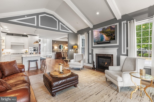 living room with lofted ceiling with beams, light hardwood / wood-style floors, a premium fireplace, and sink