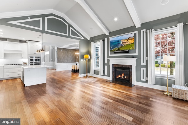 unfurnished living room with a premium fireplace, lofted ceiling with beams, and light wood-type flooring