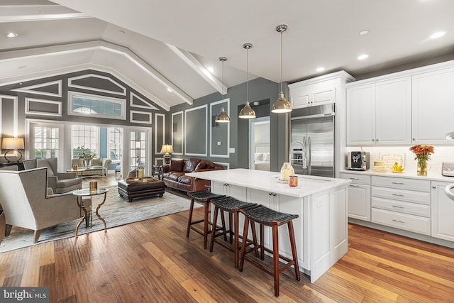 kitchen with a center island with sink, light hardwood / wood-style floors, white cabinetry, hanging light fixtures, and built in fridge