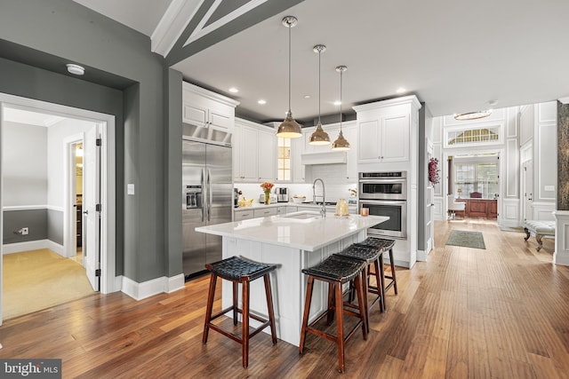 kitchen featuring white cabinets, decorative light fixtures, an island with sink, and appliances with stainless steel finishes