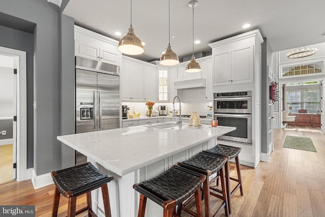 kitchen with decorative light fixtures, light stone countertops, white cabinetry, and appliances with stainless steel finishes