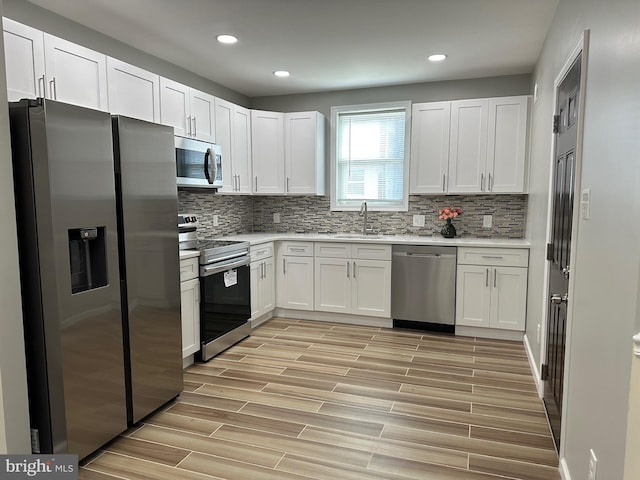 kitchen with light hardwood / wood-style floors, tasteful backsplash, sink, white cabinetry, and stainless steel appliances