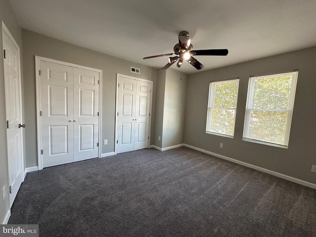 unfurnished bedroom with dark colored carpet, multiple closets, and ceiling fan