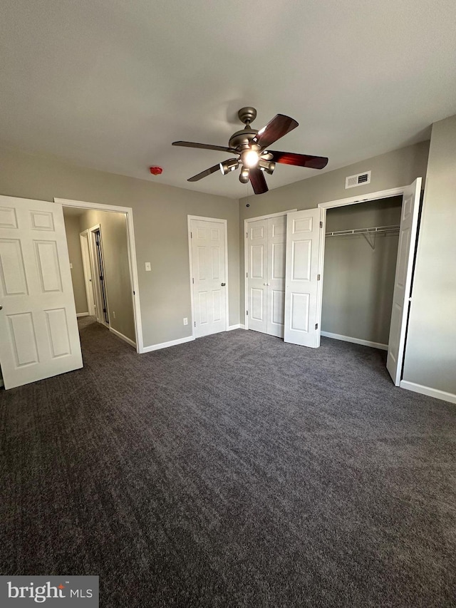 unfurnished bedroom featuring two closets, dark colored carpet, and ceiling fan