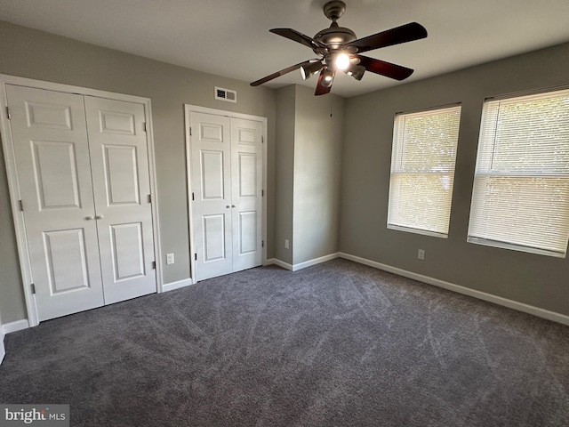 unfurnished bedroom featuring ceiling fan, multiple closets, and dark colored carpet