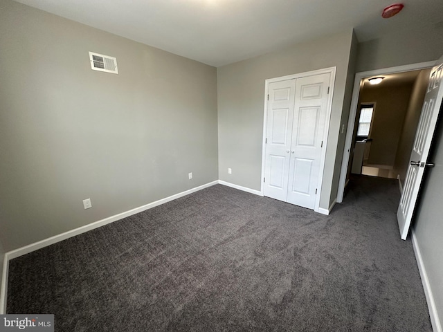 unfurnished bedroom featuring dark carpet and a closet