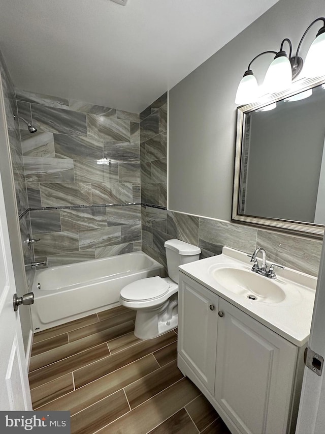 full bathroom featuring tiled shower / bath, vanity, tile walls, and toilet