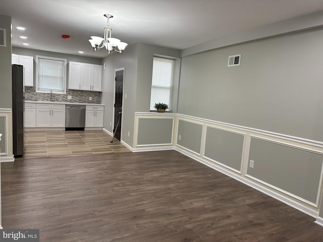 kitchen with white cabinets, hanging light fixtures, appliances with stainless steel finishes, dark hardwood / wood-style flooring, and decorative backsplash