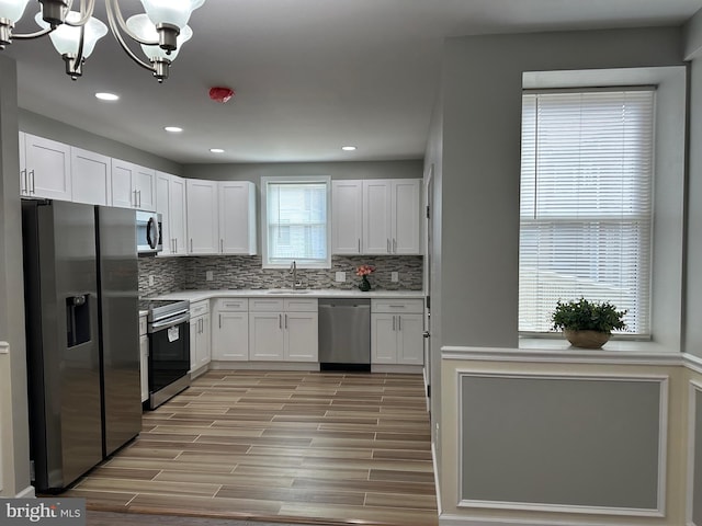 kitchen with appliances with stainless steel finishes, a healthy amount of sunlight, white cabinetry, and pendant lighting