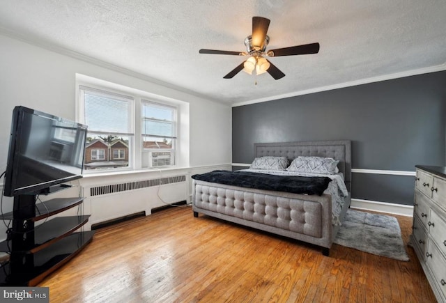 bedroom with crown molding, light hardwood / wood-style floors, ceiling fan, and radiator heating unit