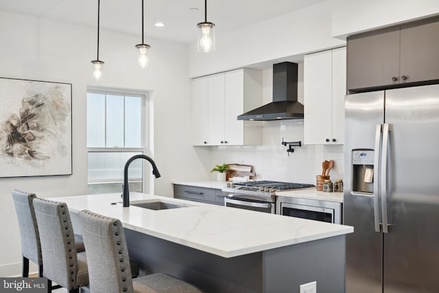 kitchen featuring a kitchen island with sink, sink, hanging light fixtures, wall chimney exhaust hood, and stainless steel appliances