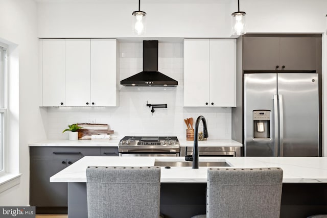 kitchen featuring appliances with stainless steel finishes, wall chimney exhaust hood, pendant lighting, and white cabinets