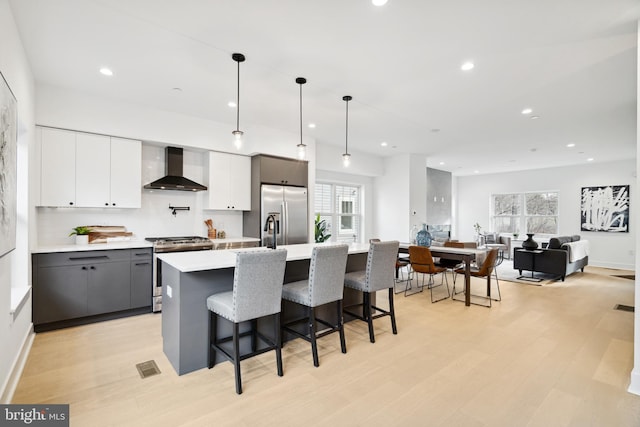 kitchen with gray cabinets, plenty of natural light, hanging light fixtures, wall chimney exhaust hood, and appliances with stainless steel finishes