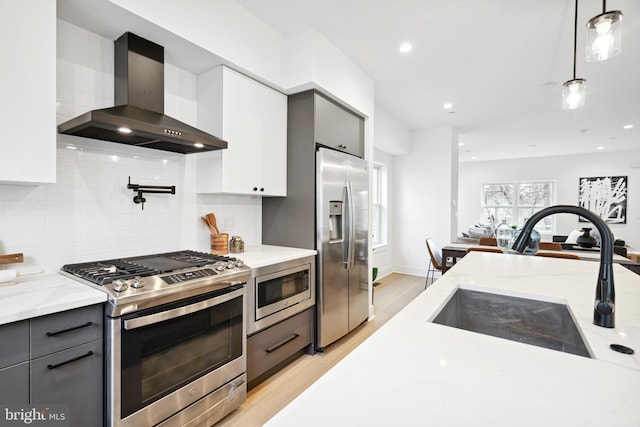 kitchen featuring gray cabinetry, stainless steel appliances, hanging light fixtures, and wall chimney range hood