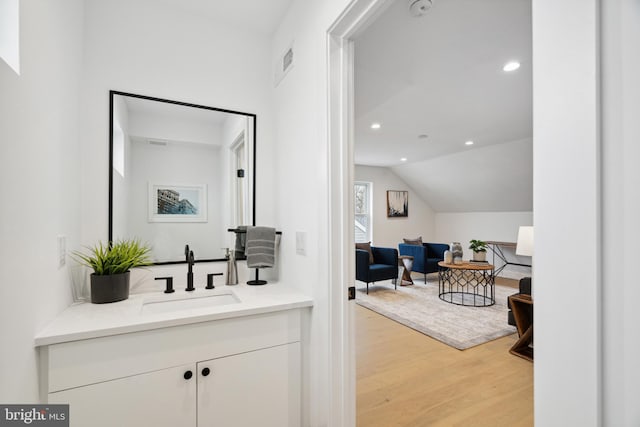 interior space with vaulted ceiling, vanity, and hardwood / wood-style floors