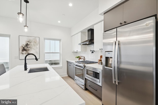 kitchen with white cabinets, pendant lighting, stainless steel appliances, sink, and wall chimney range hood