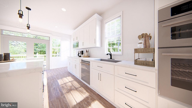 kitchen with white cabinets, pendant lighting, sink, stainless steel appliances, and light wood-type flooring