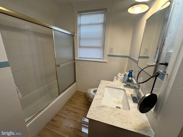 full bathroom featuring toilet, vanity, hardwood / wood-style floors, tile walls, and enclosed tub / shower combo