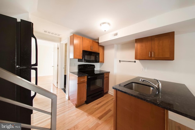 kitchen featuring light wood-type flooring, black appliances, dark stone counters, and sink