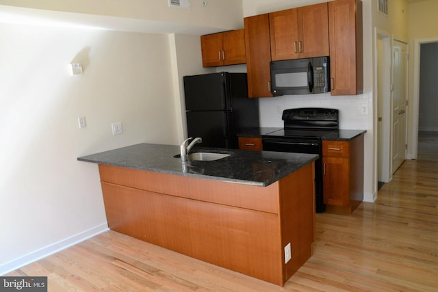 kitchen with light wood-type flooring, black appliances, kitchen peninsula, and sink