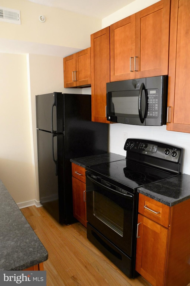 kitchen featuring dark stone countertops, light hardwood / wood-style floors, and black appliances