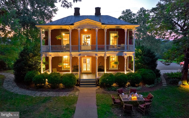 view of front of home featuring covered porch, a front lawn, a balcony, and an outdoor fire pit