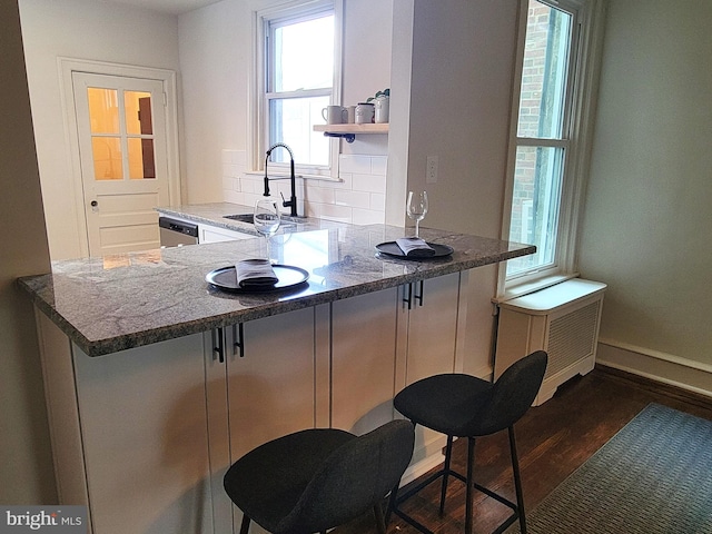 kitchen featuring sink, a kitchen bar, decorative backsplash, dark stone countertops, and stainless steel dishwasher