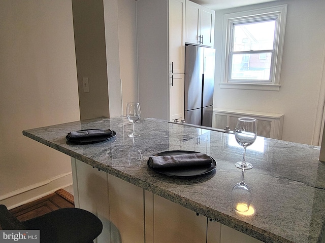 kitchen with dark stone countertops, white cabinets, a kitchen bar, and stainless steel fridge