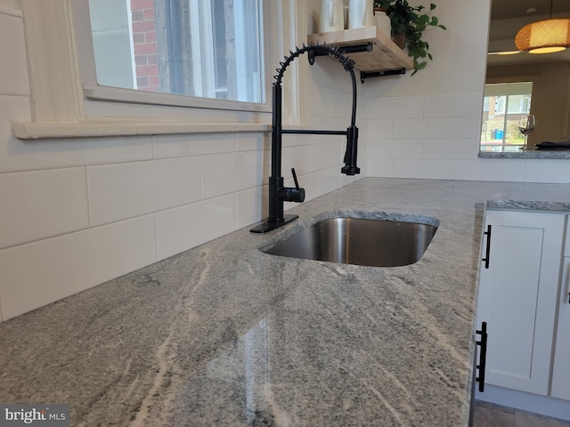 details featuring light stone countertops, white cabinets, tasteful backsplash, and sink