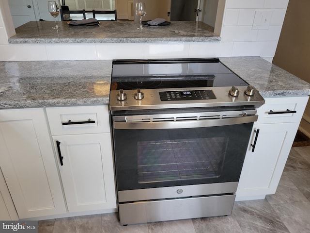 kitchen featuring stainless steel range, stone countertops, decorative backsplash, and white cabinetry