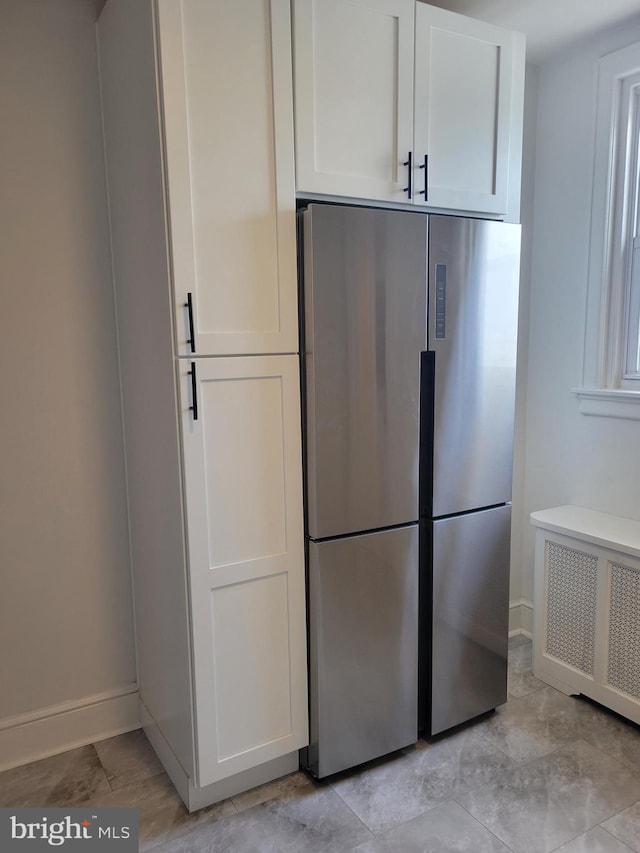 kitchen with radiator, stainless steel refrigerator, and white cabinets