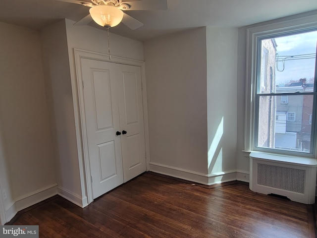 unfurnished bedroom featuring a closet, radiator, ceiling fan, and dark hardwood / wood-style flooring