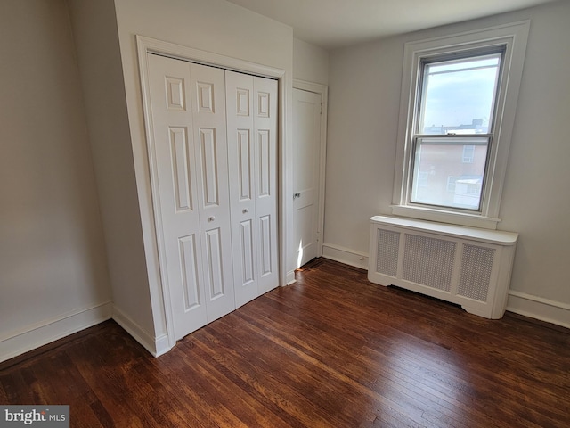 unfurnished bedroom featuring dark hardwood / wood-style floors, radiator heating unit, and a closet