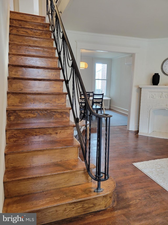 stairway with an AC wall unit, a fireplace, hardwood / wood-style floors, and crown molding