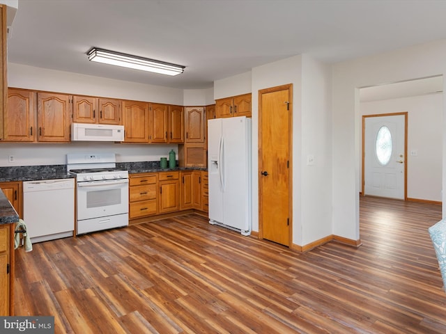 kitchen with dark wood-type flooring, white appliances, and dark stone countertops