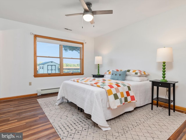 bedroom featuring hardwood / wood-style floors, a baseboard heating unit, and ceiling fan