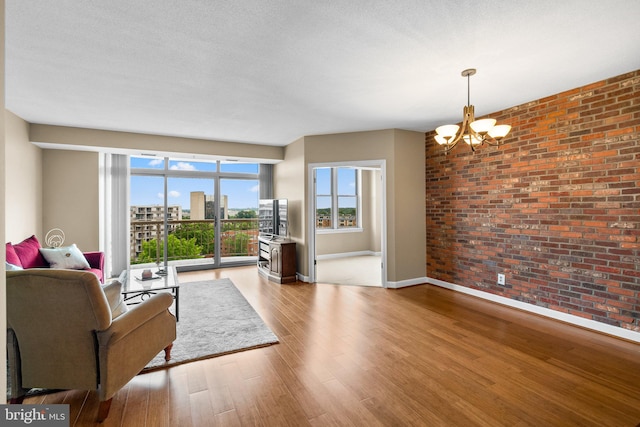 living room with light wood-type flooring, brick wall, a textured ceiling, and a notable chandelier