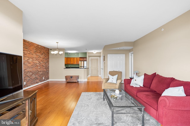 living room featuring light hardwood / wood-style flooring, a notable chandelier, and brick wall