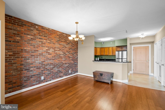 unfurnished living room with brick wall, a chandelier, and hardwood / wood-style flooring