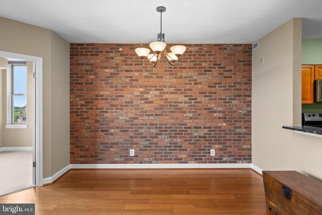 unfurnished dining area with a chandelier, brick wall, and hardwood / wood-style flooring