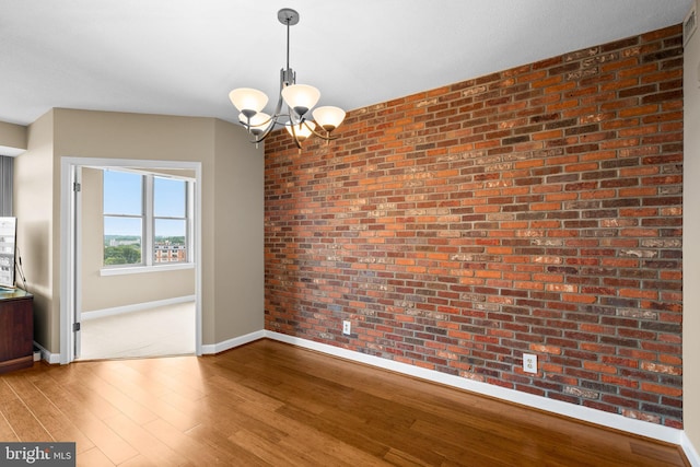 unfurnished room featuring an inviting chandelier, wood-type flooring, and brick wall