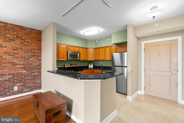 kitchen with a textured ceiling, sink, kitchen peninsula, stainless steel appliances, and brick wall