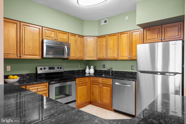 kitchen featuring dark stone countertops, a textured ceiling, appliances with stainless steel finishes, and light tile patterned floors