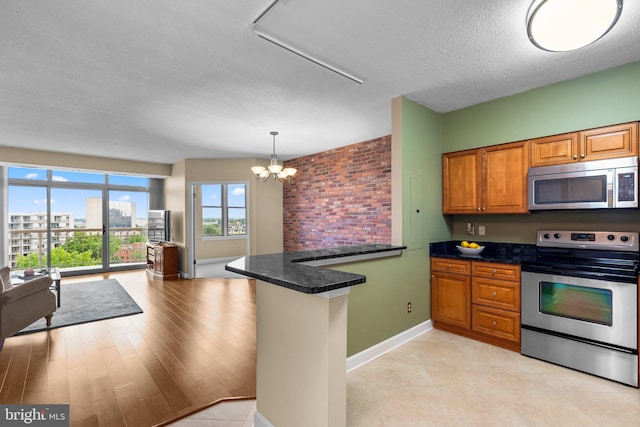 kitchen featuring appliances with stainless steel finishes, hanging light fixtures, kitchen peninsula, light wood-type flooring, and an inviting chandelier