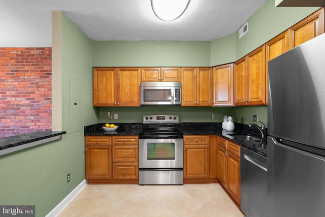 kitchen with a textured ceiling, dark stone counters, sink, and stainless steel appliances