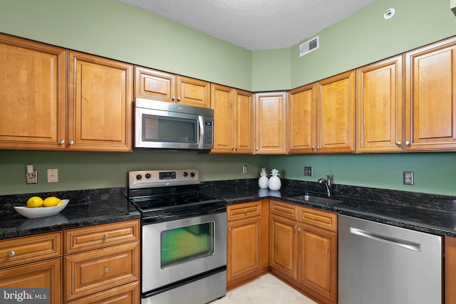 kitchen featuring dark stone counters, a textured ceiling, appliances with stainless steel finishes, and sink