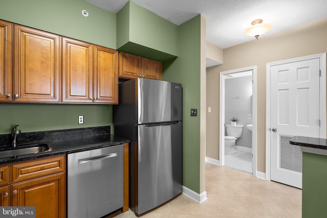 kitchen with appliances with stainless steel finishes, light tile patterned floors, a textured ceiling, dark stone counters, and sink